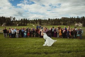 Wedding celebration in open field with large group of guests and mountain scenery.