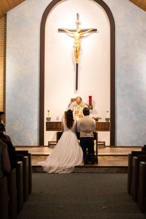 A couple stands at the altar beneath a crucifix during their church wedding ceremony.