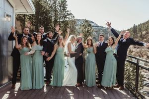 Wedding party in teal dresses and black suits poses on mountain deck.