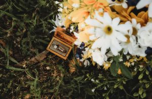 A vintage wooden ring box nestled among white and orange flowers on grass.