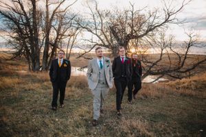 Grooms walks along a hilltop path at sunset with bare trees and golden grasses in the moody autumn landscape.