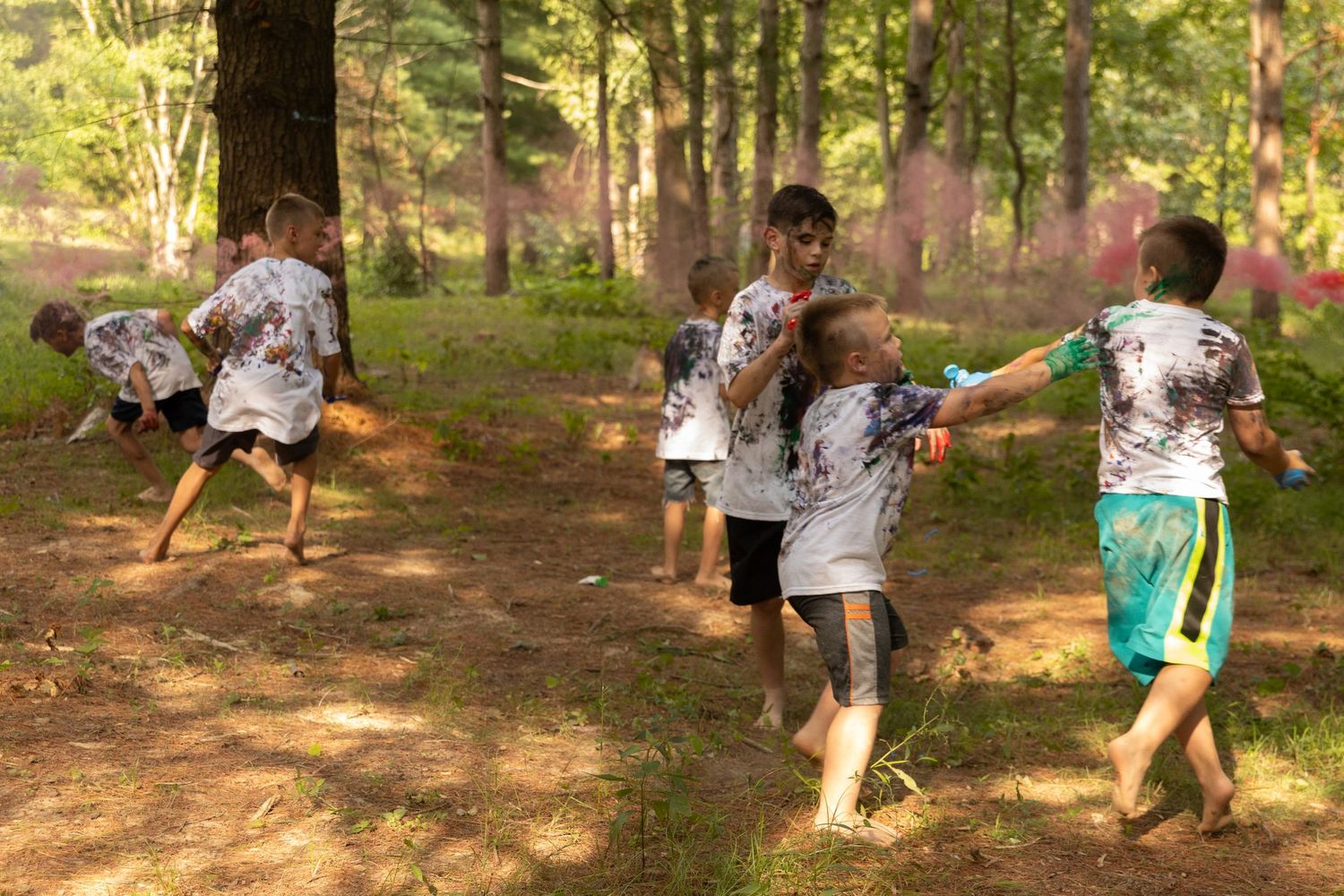 A friend group of boys having a paint fight in the middle of a pine forest in the Illinois summer.