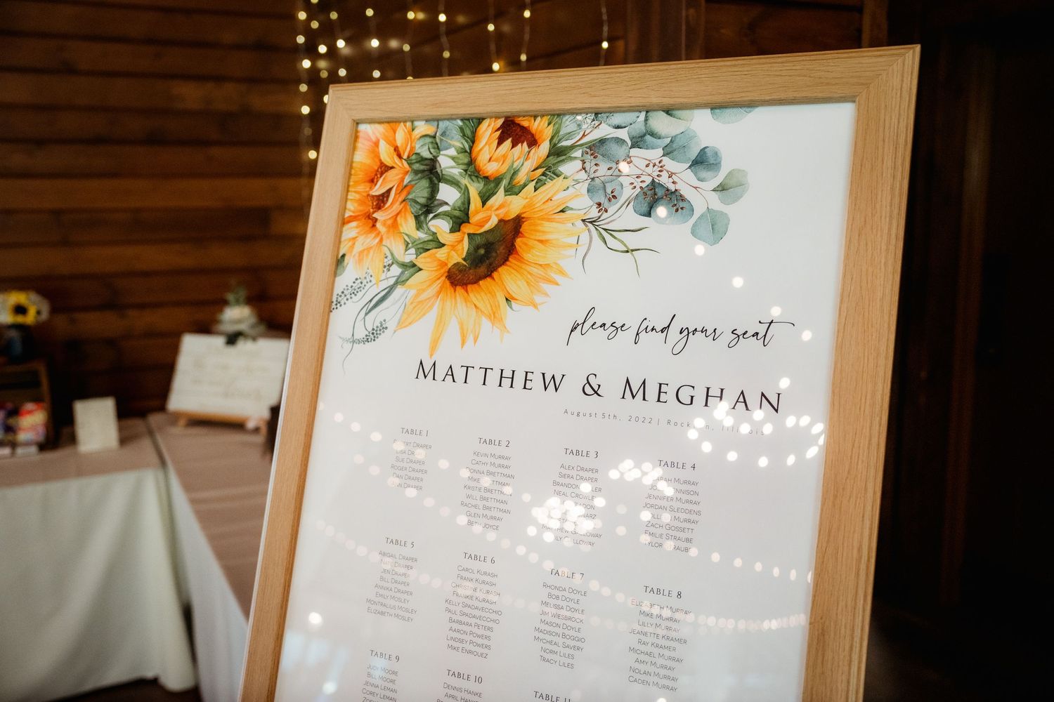 Elegant seating chart with sunflower design in wooden frame at wedding reception.