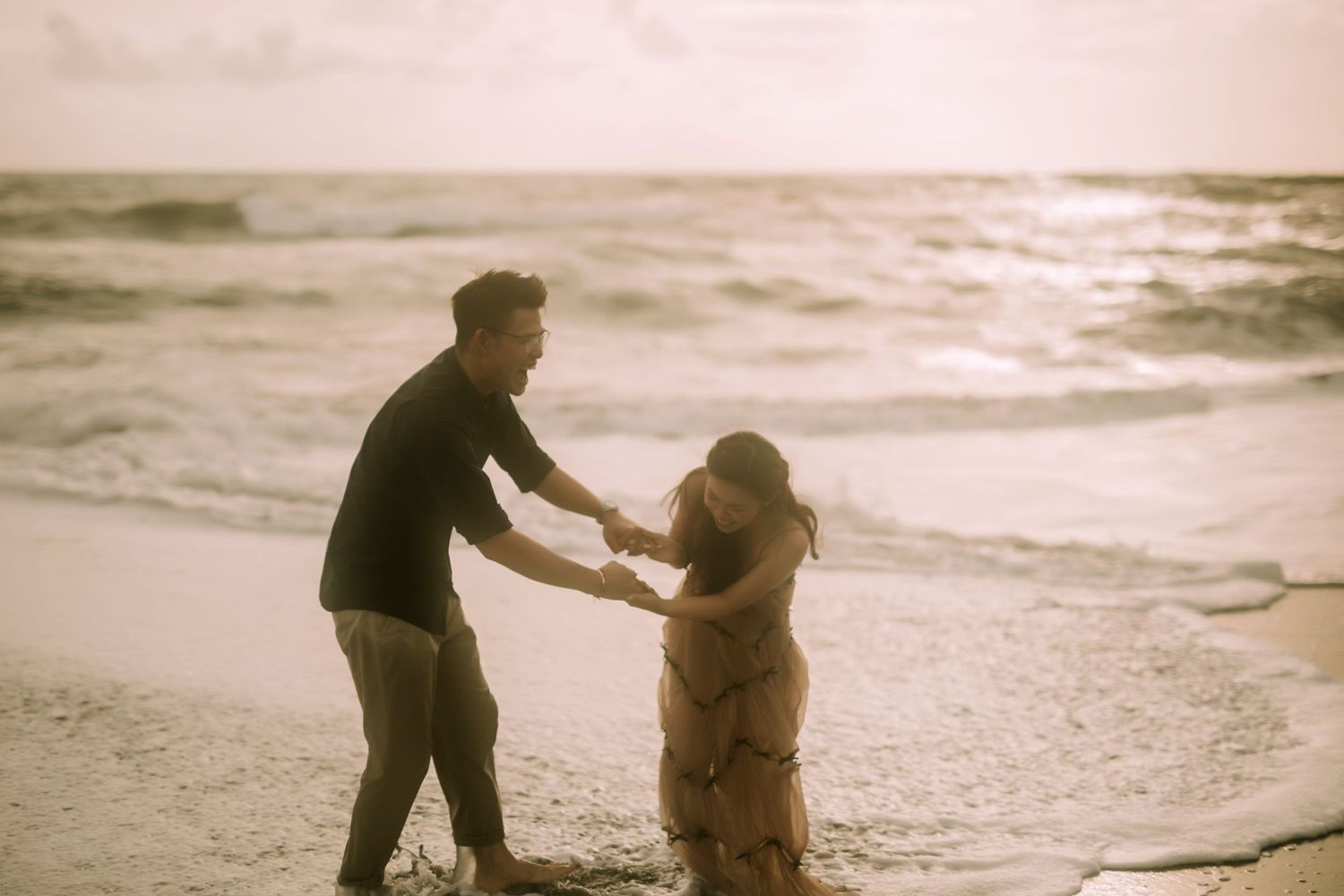 Two figures share tender moments on a misty beach at sunset.