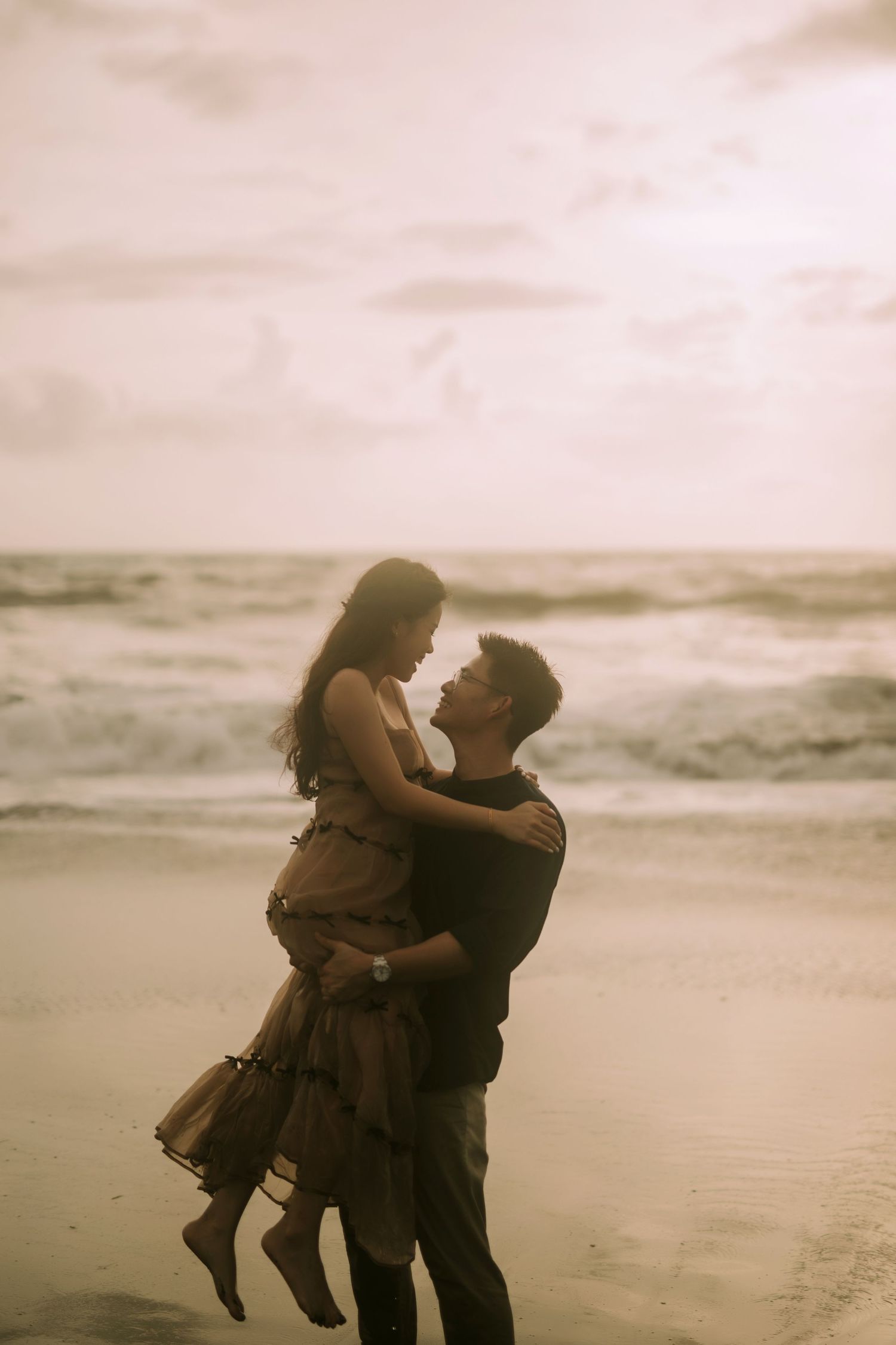 A couple embraces passionately on a serene beach with gentle waves in the background.