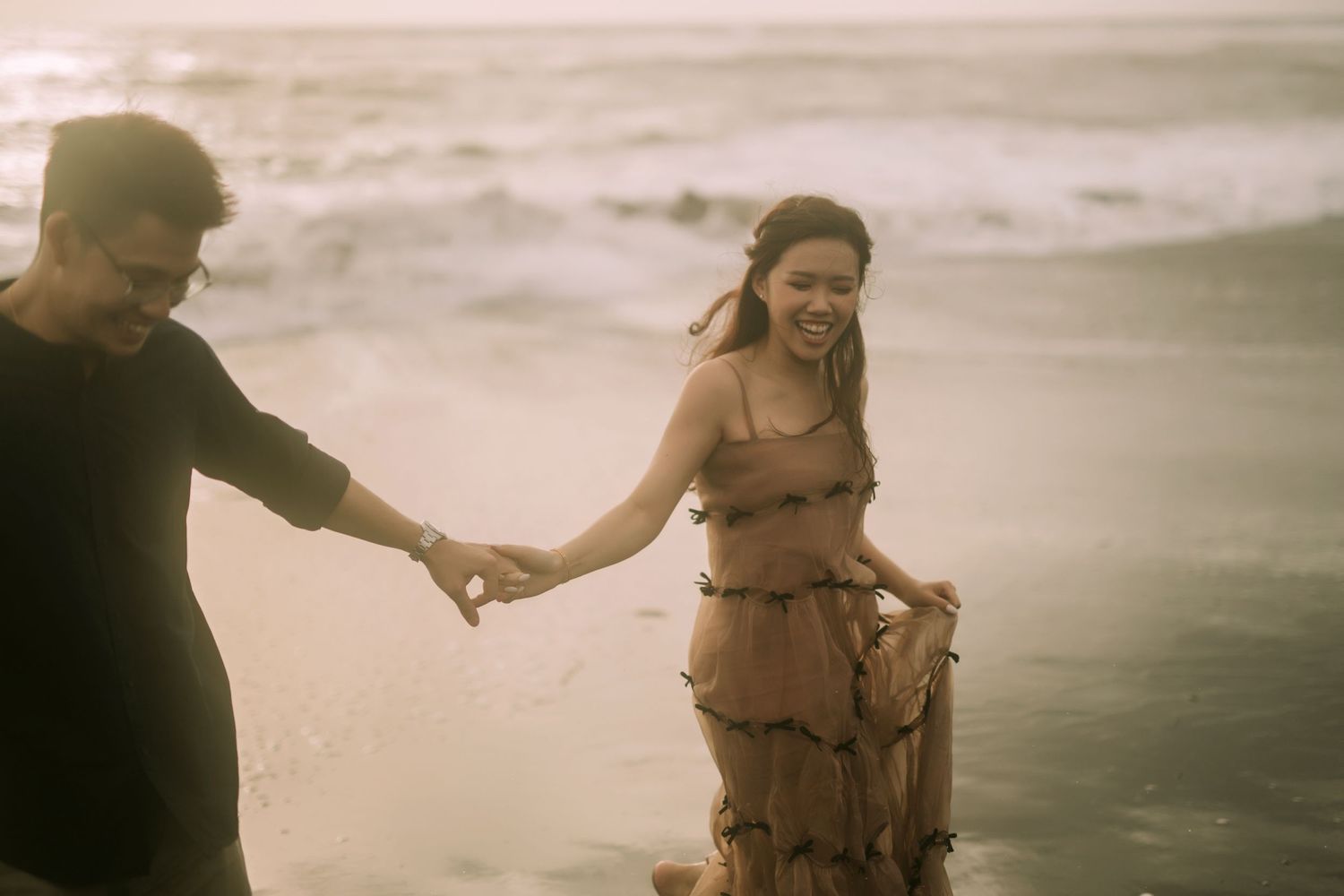 Two people hold hands and dance together on a moody oceanfront.
