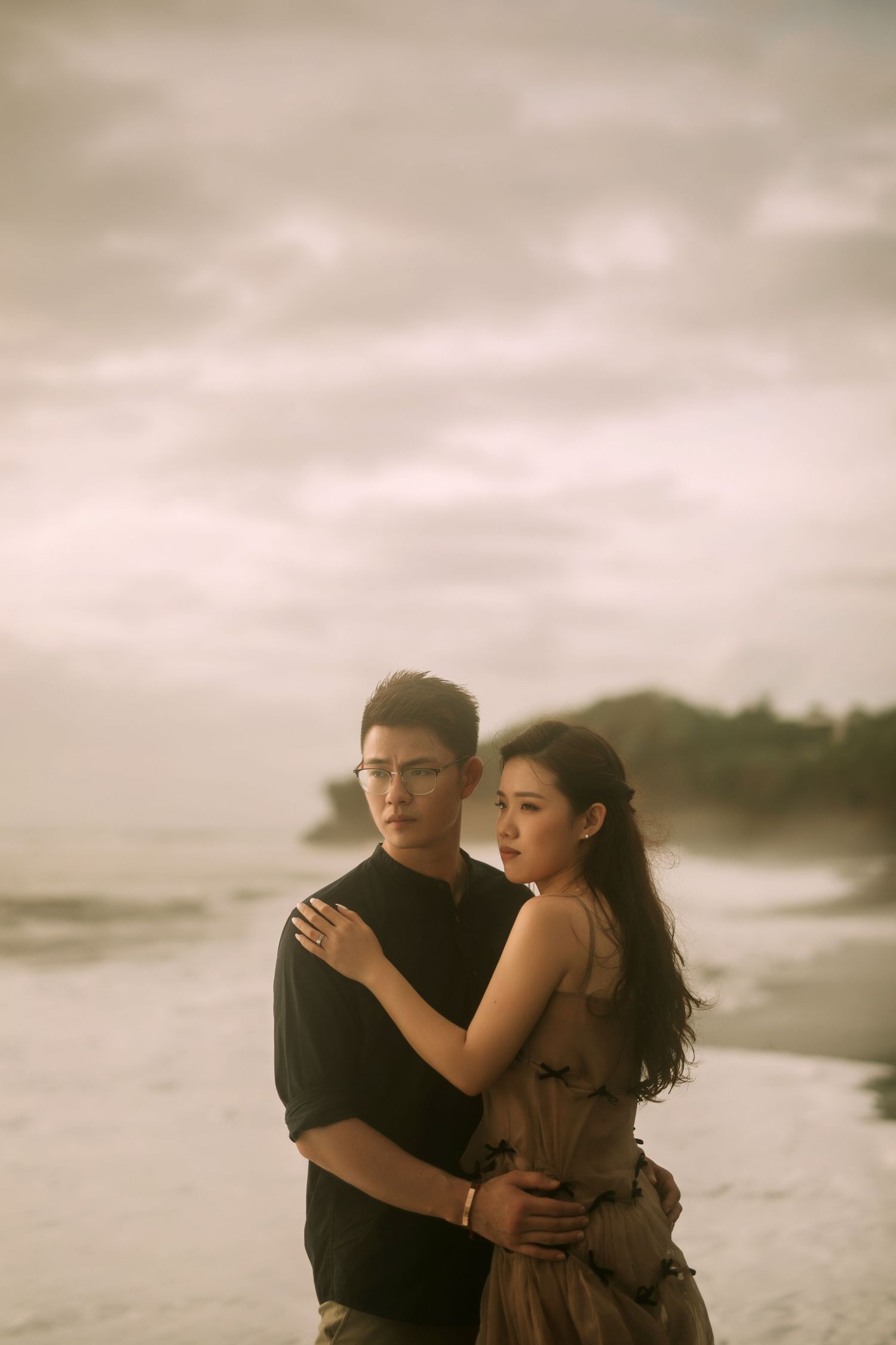 Couple shares intimate moments on a misty beach with dramatic cloudy skies.