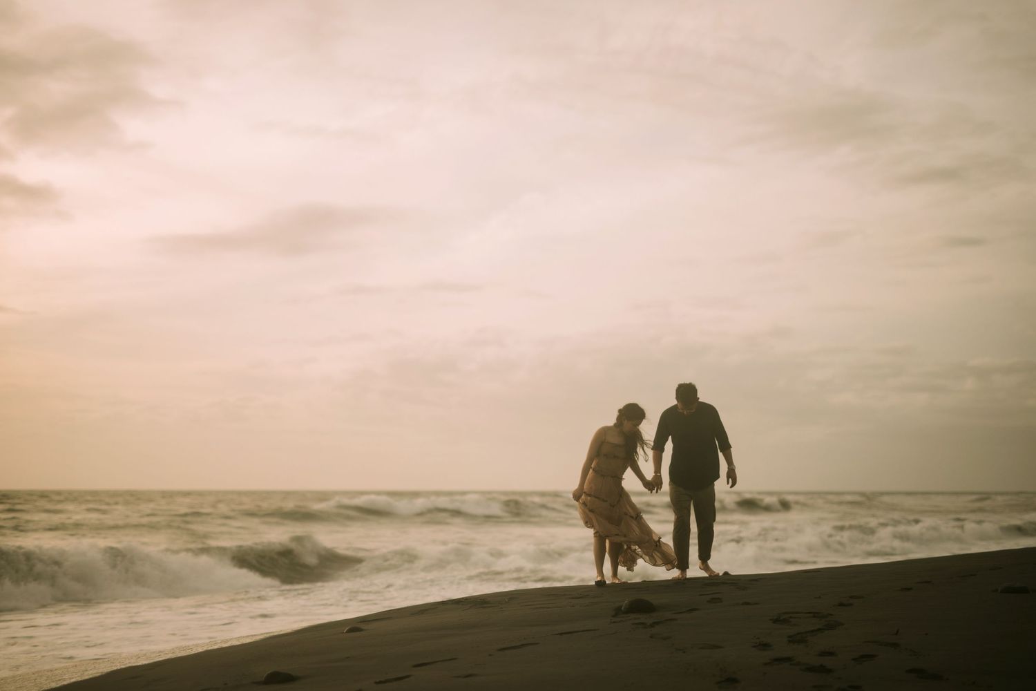Silhouettes of two people walking along a dramatic beach at sunset.