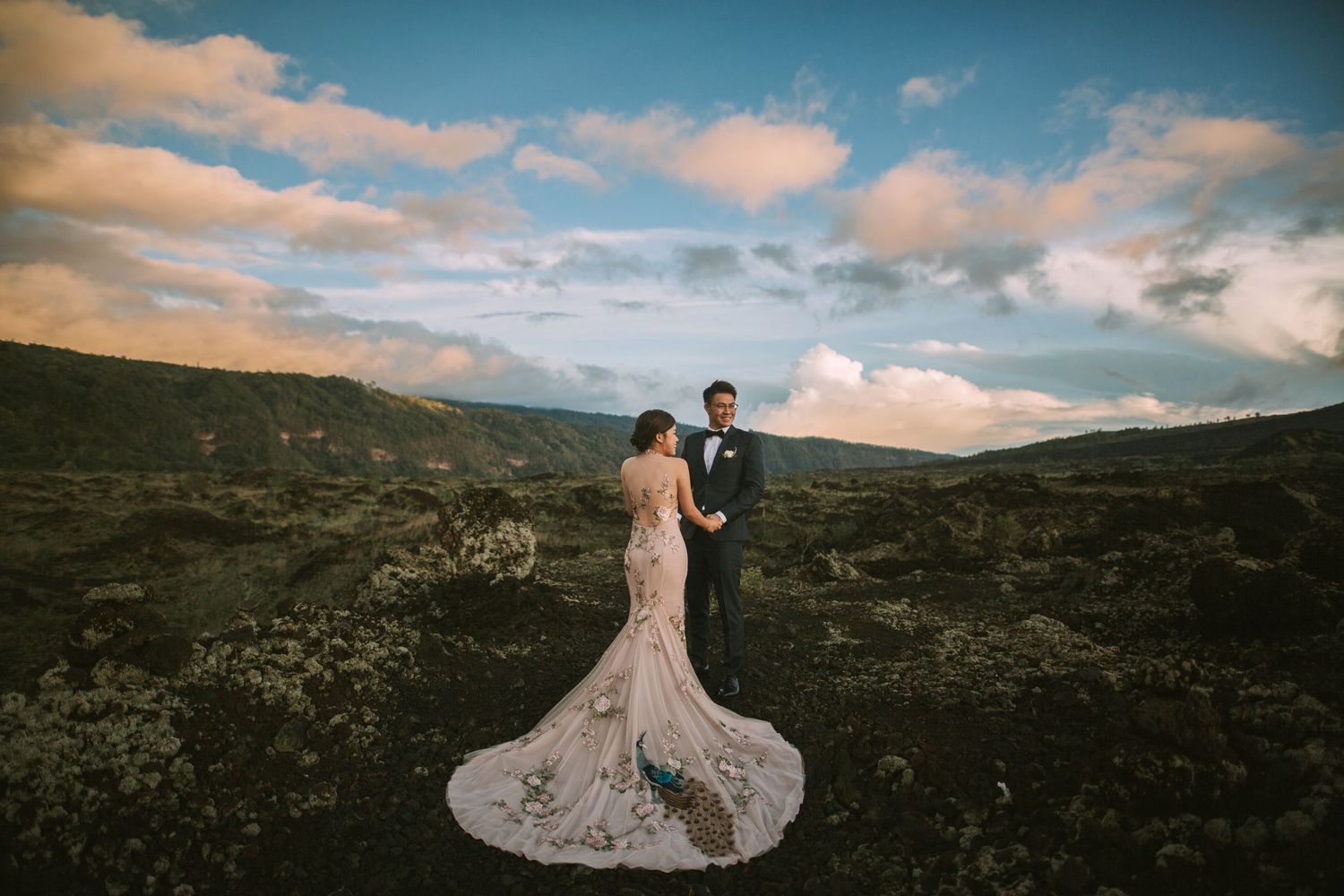 Wedding couple poses on mountainous terrain under beautiful sunset skies.