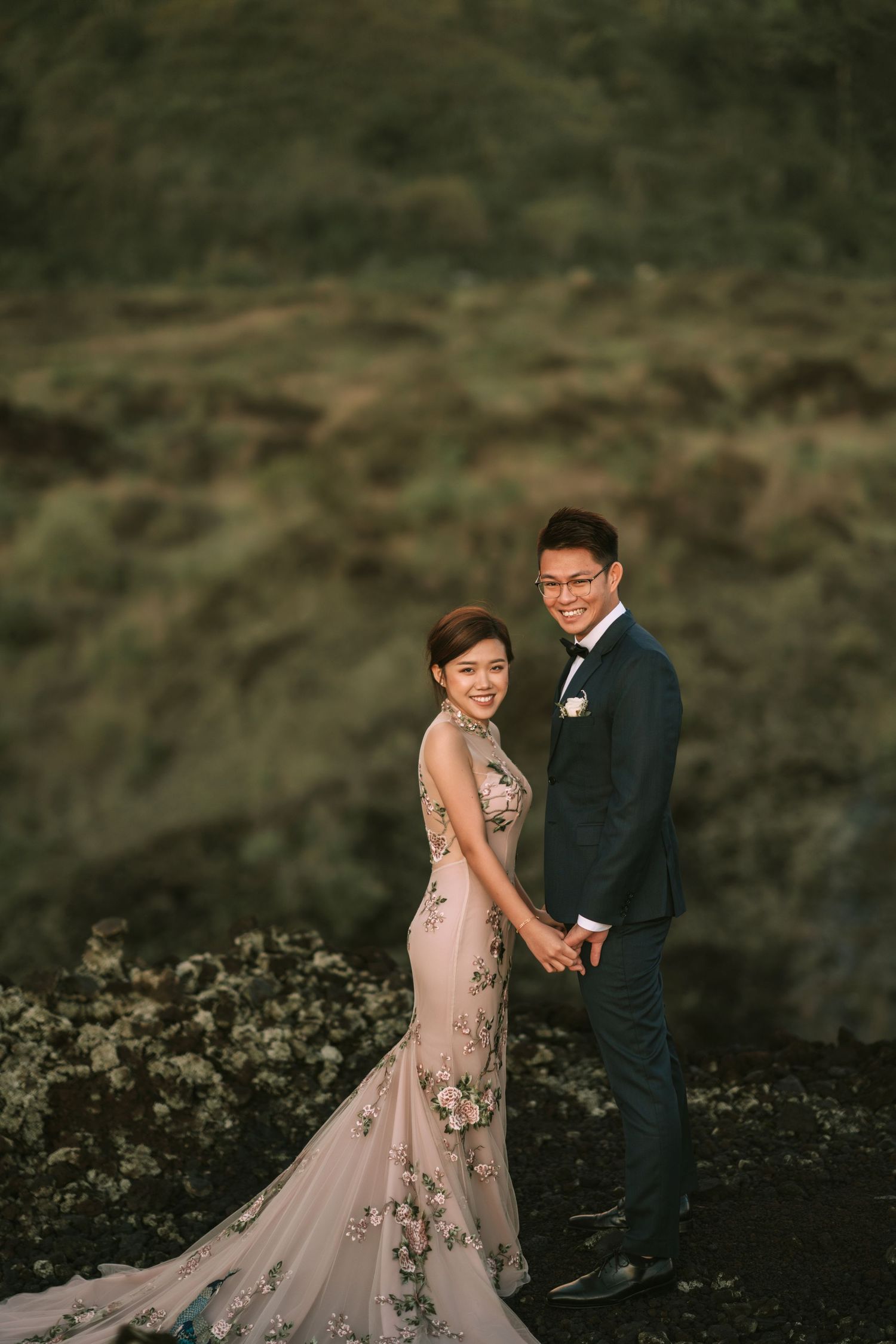 Couple in wedding attire shares playful moment on mountain landscape.