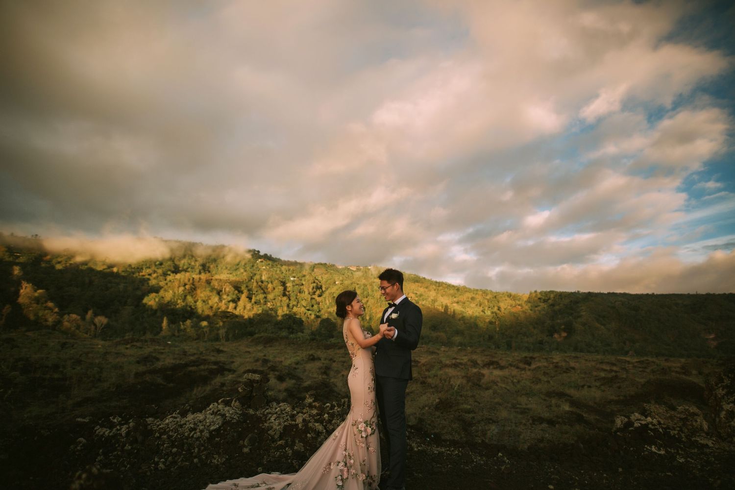 Wedding couple poses against golden mountain landscape at sunset.