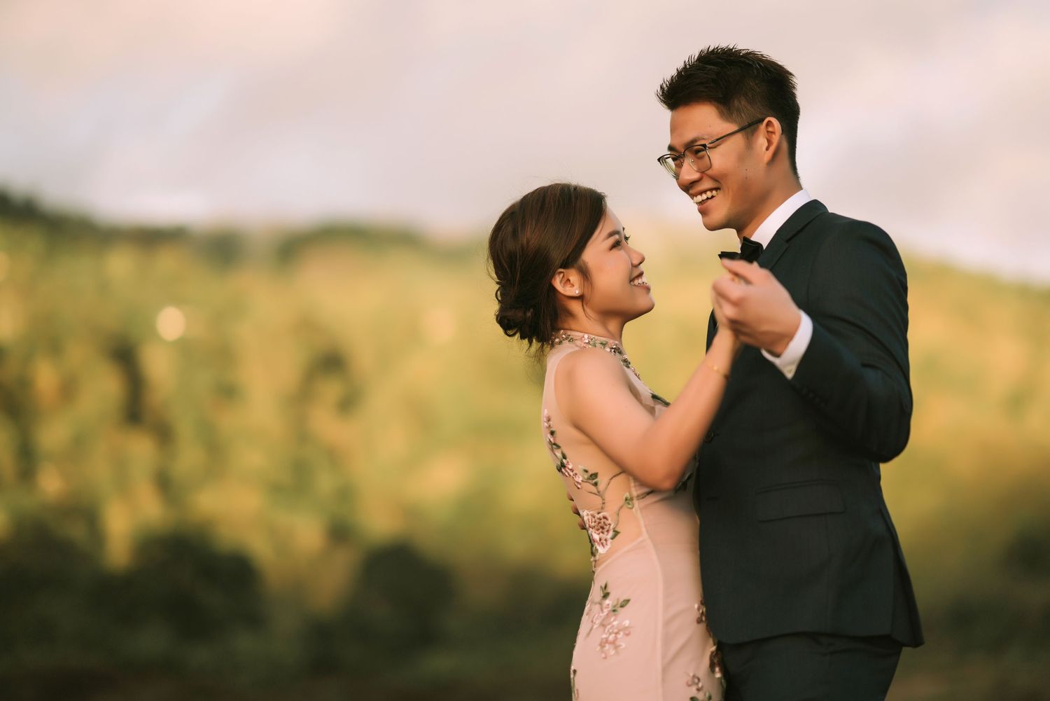 Romantic wedding couple embraces during golden hour sunset against dramatic mountain backdrop.