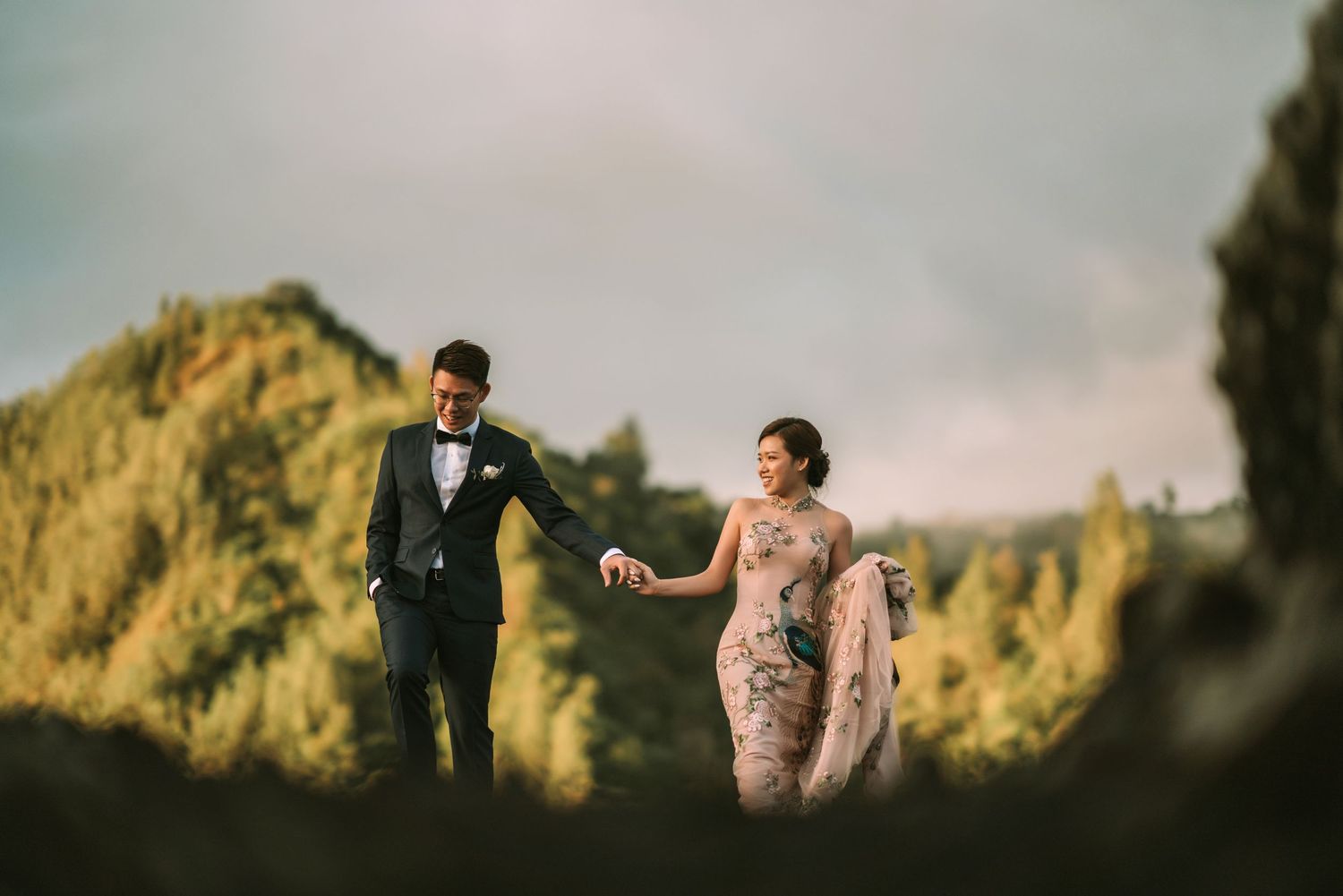 Elegant couple shares intimate moment in formal attire against mountainous landscape at dusk.