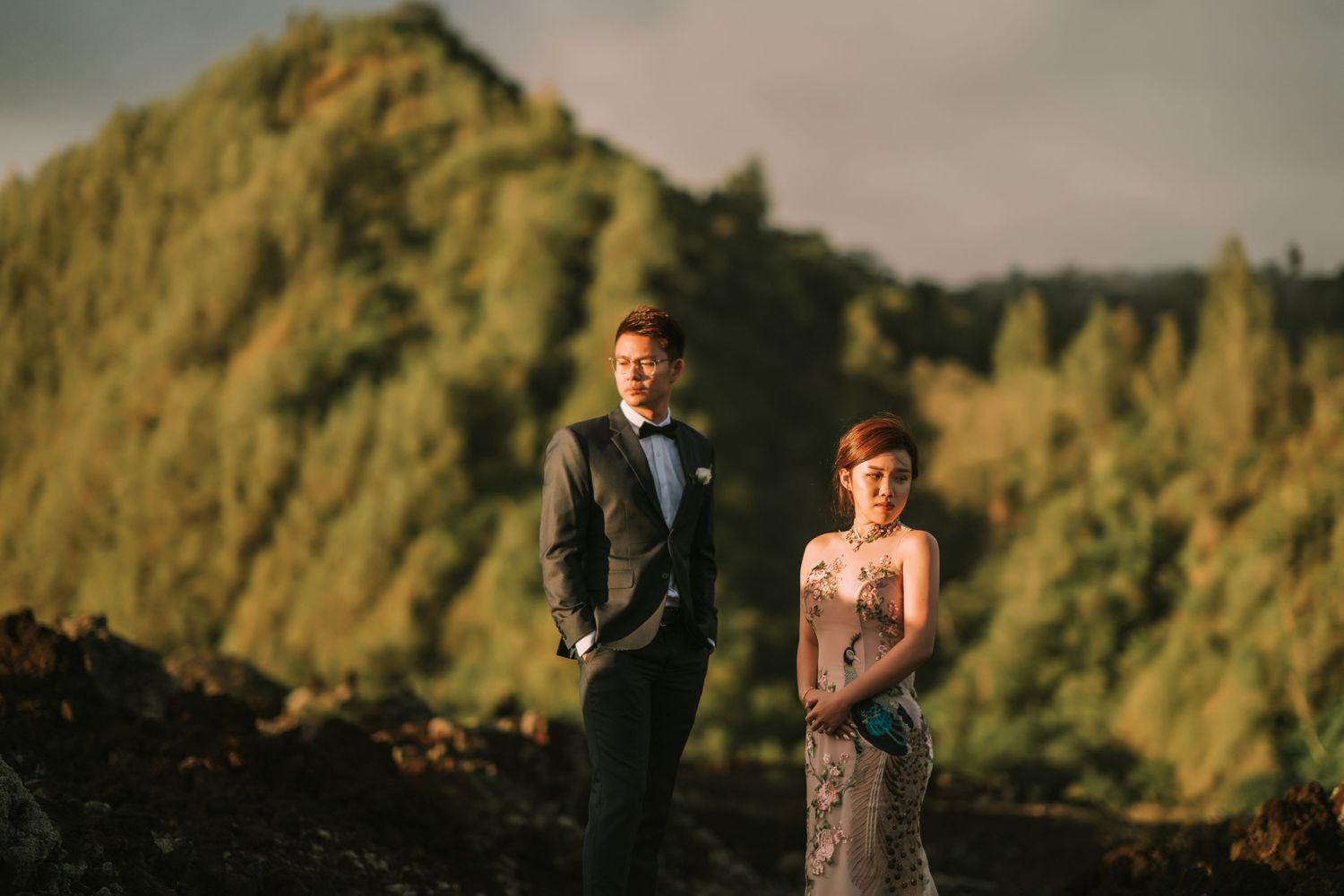 Wedding couple poses on rocky terrain during sunset with dramatic cloudy sky.