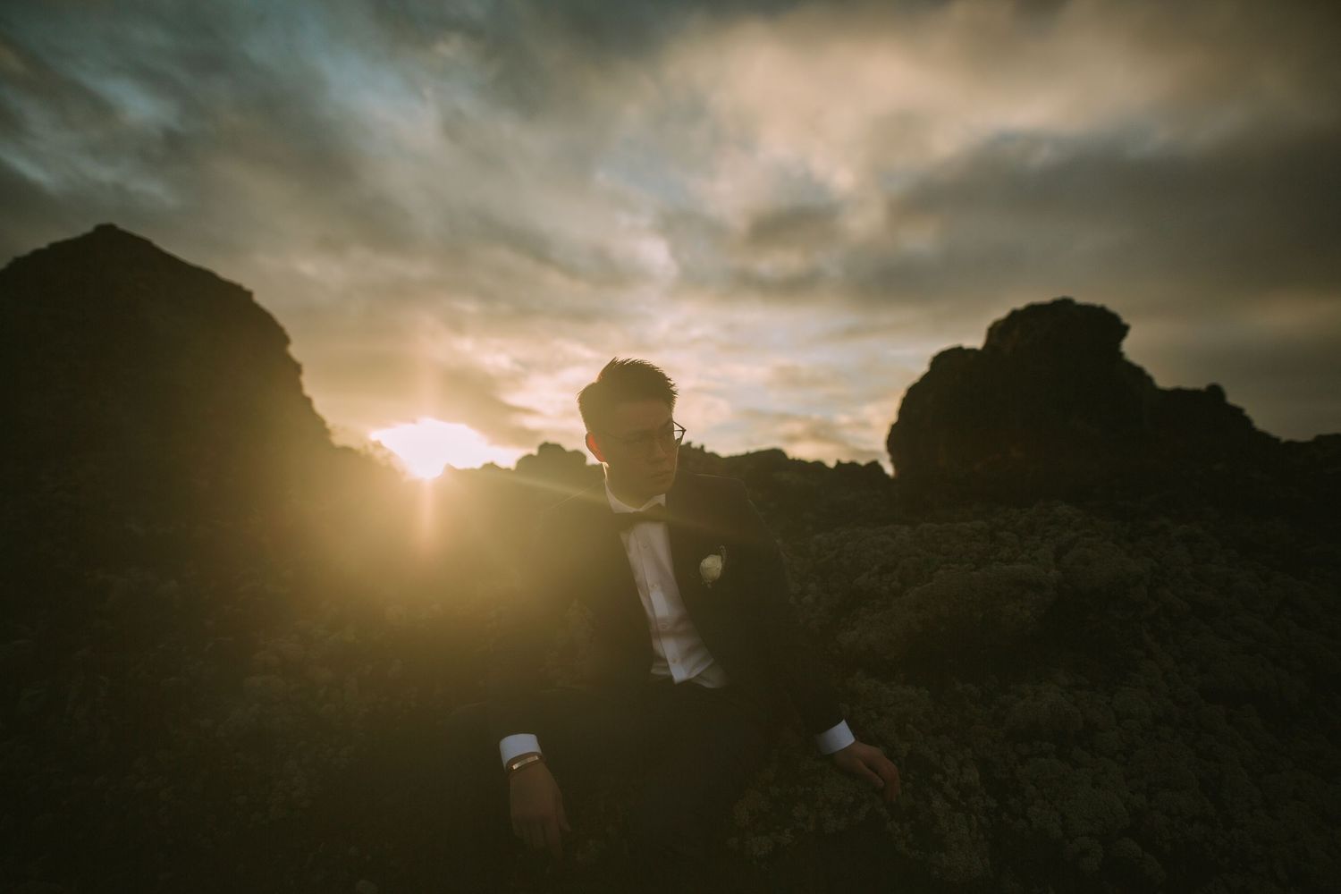 Dramatic silhouette of wedding couple against moody sunset sky and rocky terrain.