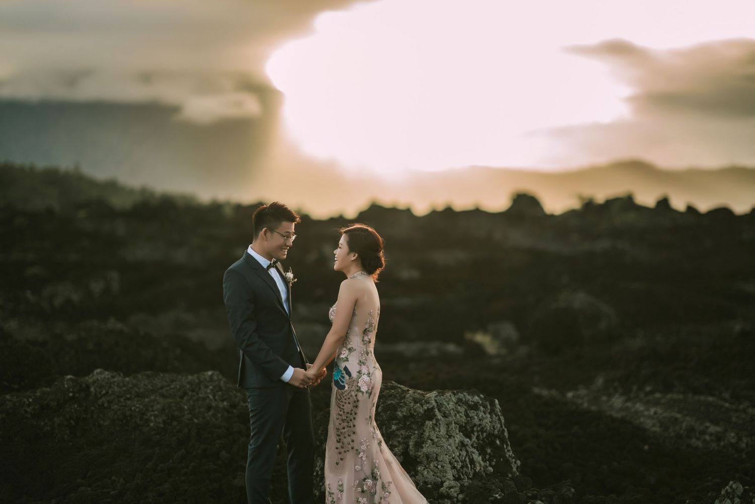 Wedding couple poses against stunning sunset mountain landscape.