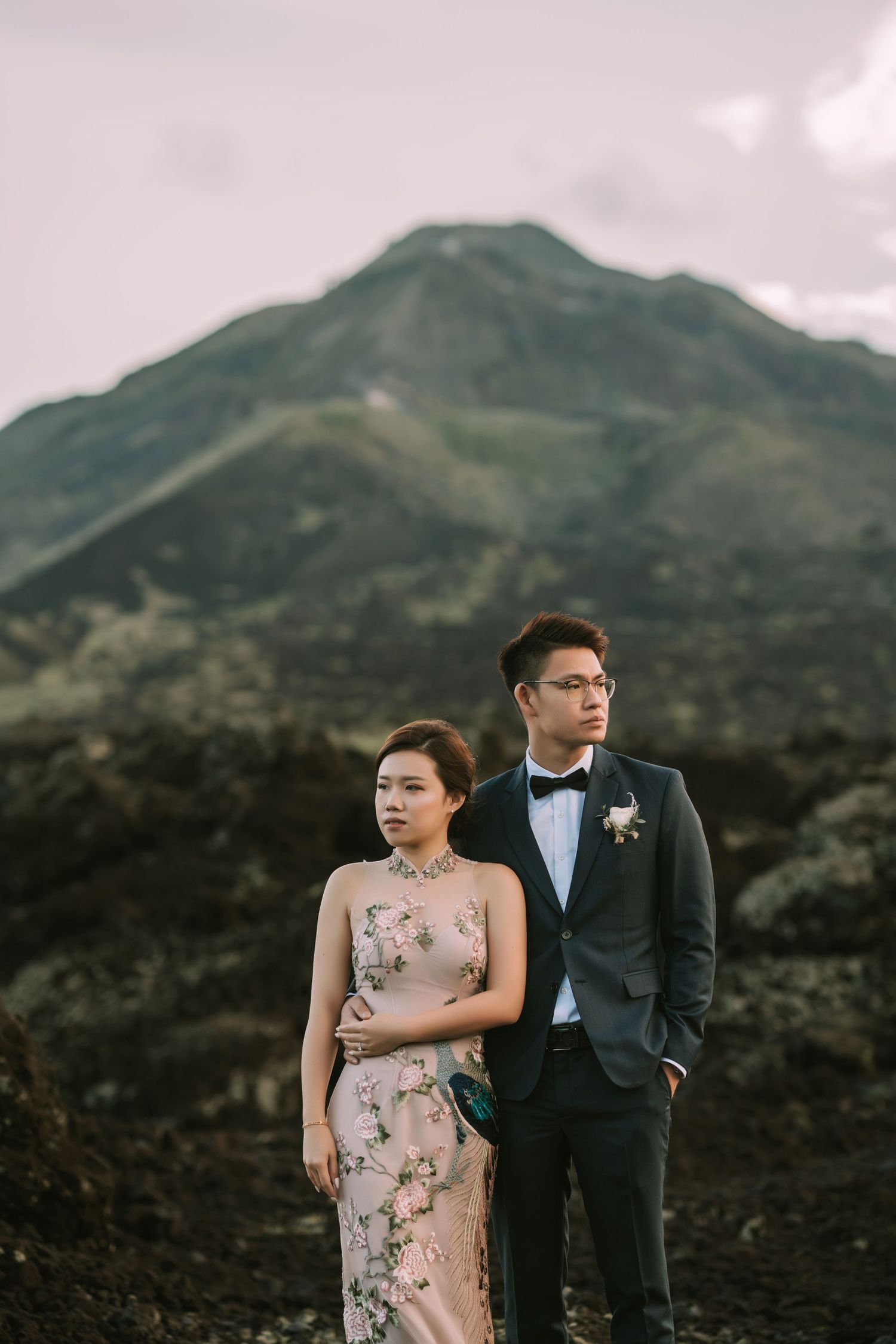 Elegant couple poses in formal wear against majestic mountain landscape.