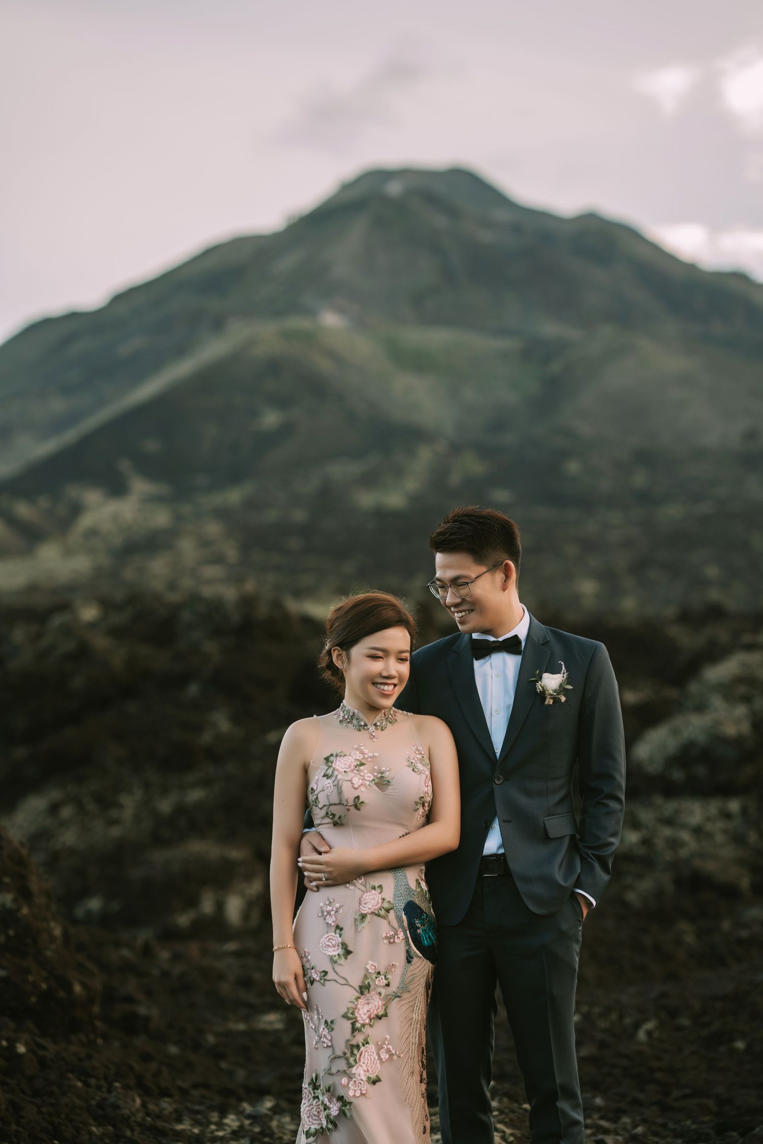 Couple shares intimate moment in formal wear with mountain backdrop.