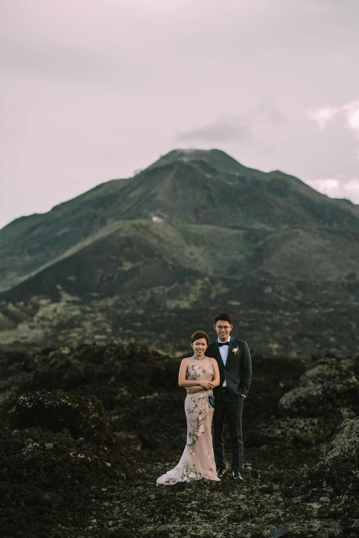 Formal portrait of couple standing before steep mountain peak.