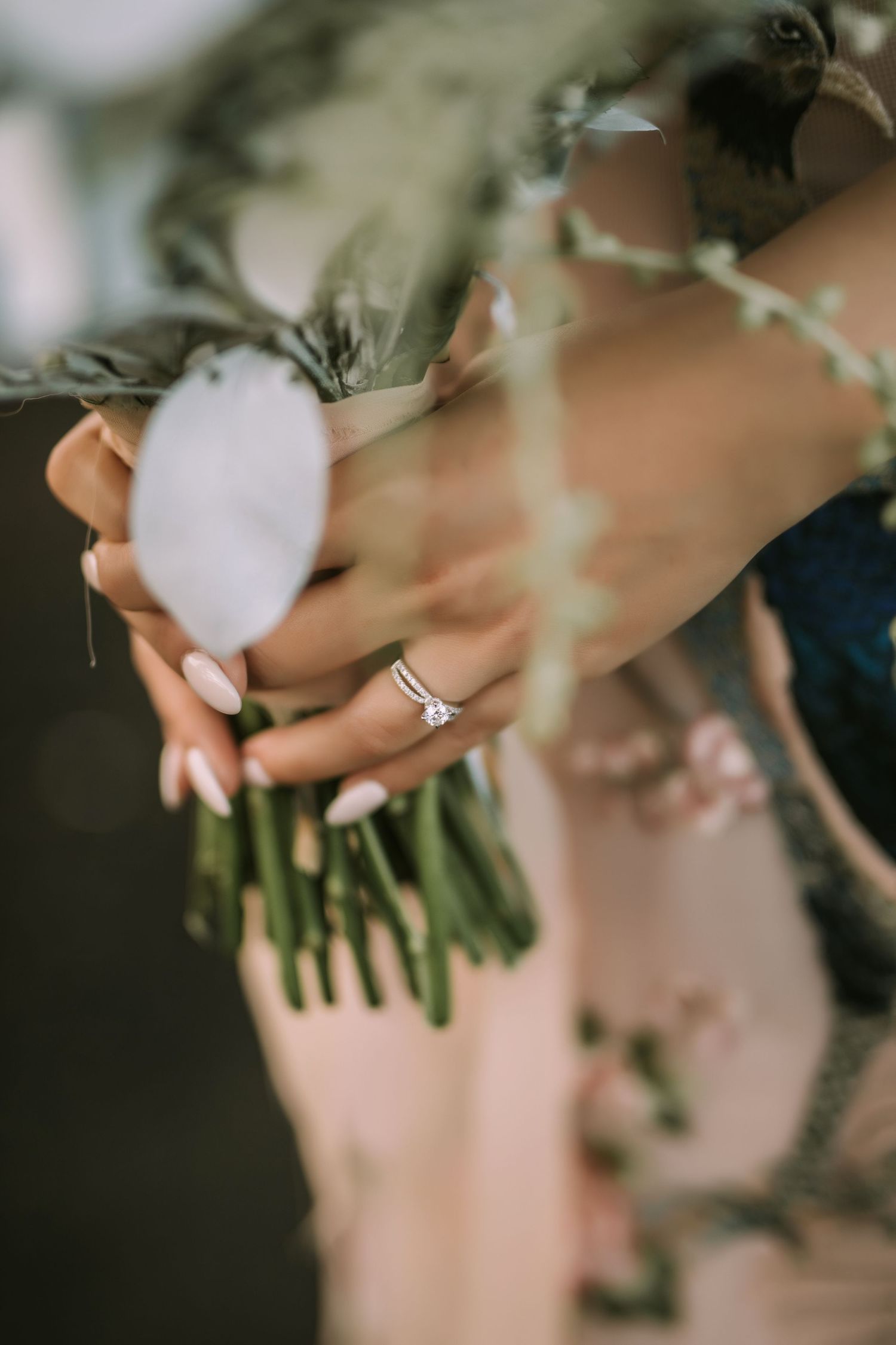 Close-up of hands holding wedding bouquet with engagement ring detail.