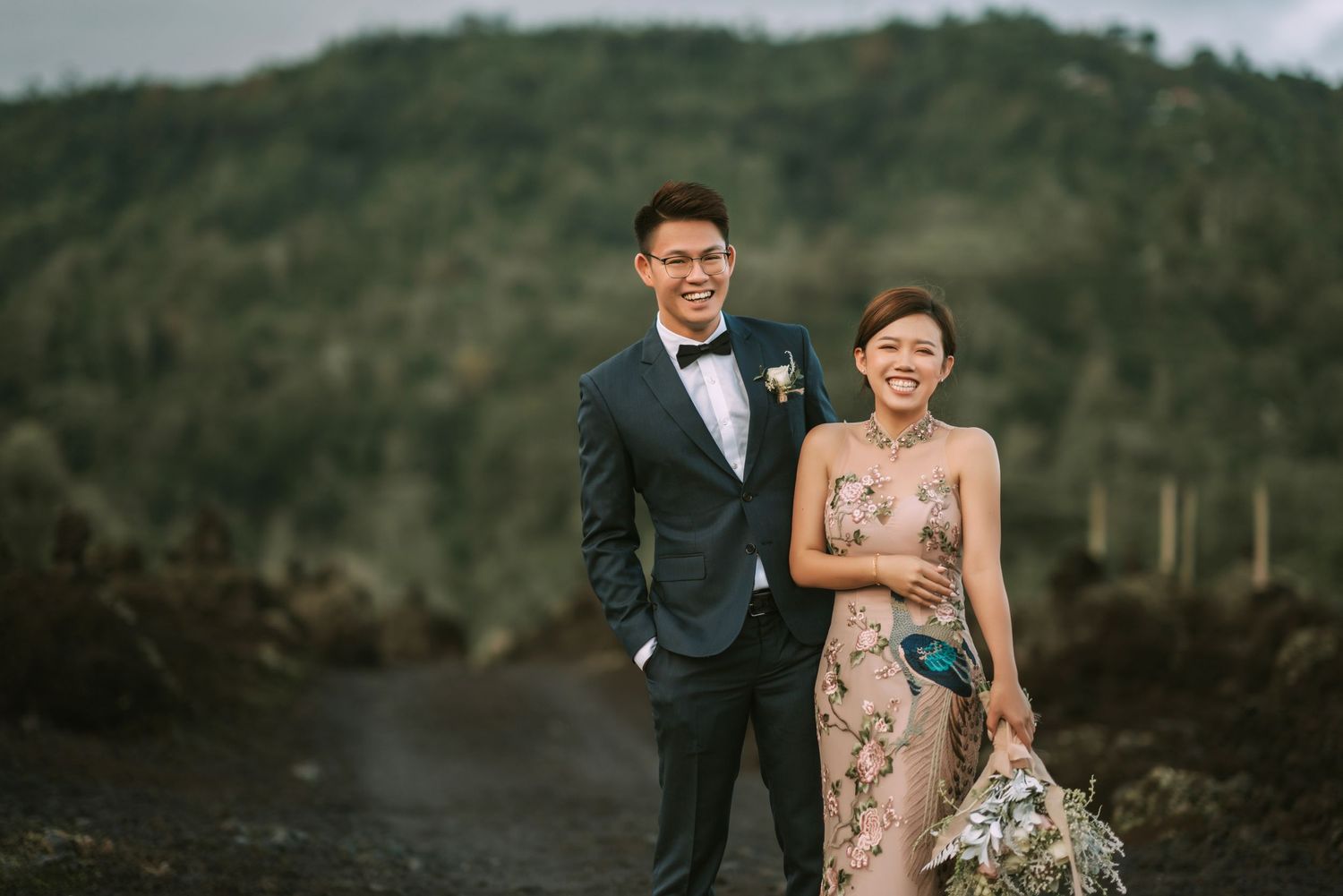 Elegant couple takes wedding photos against dramatic mountain landscape on volcanic terrain.