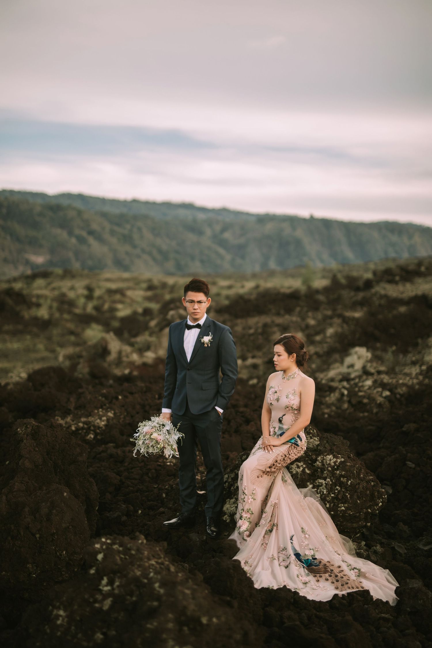 Elegant couple stands together on rocky volcanic landscape with mountains in the distance.