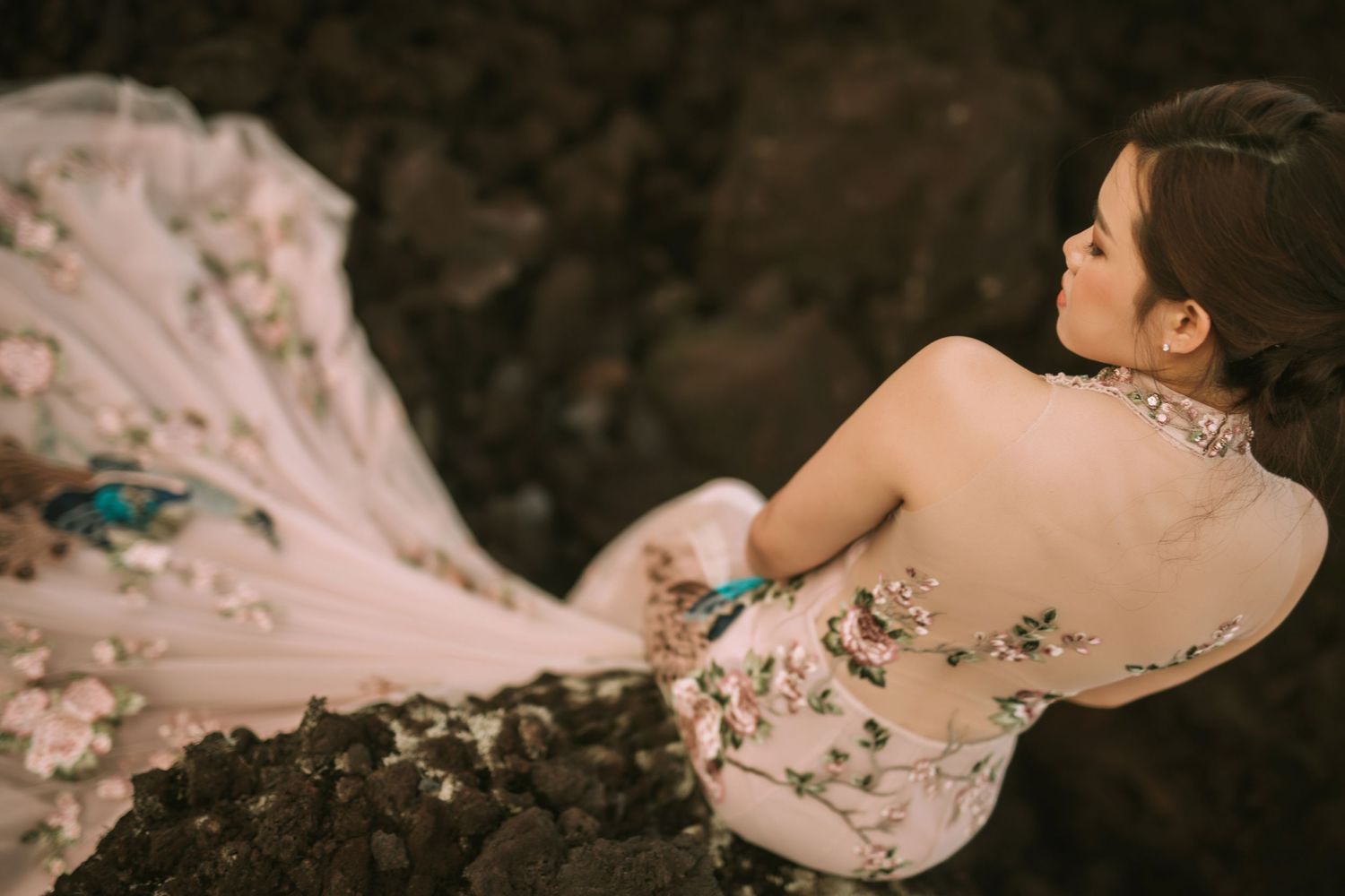 Close-up detail of pink wedding dress with floral embellishments against dark rocky terrain.