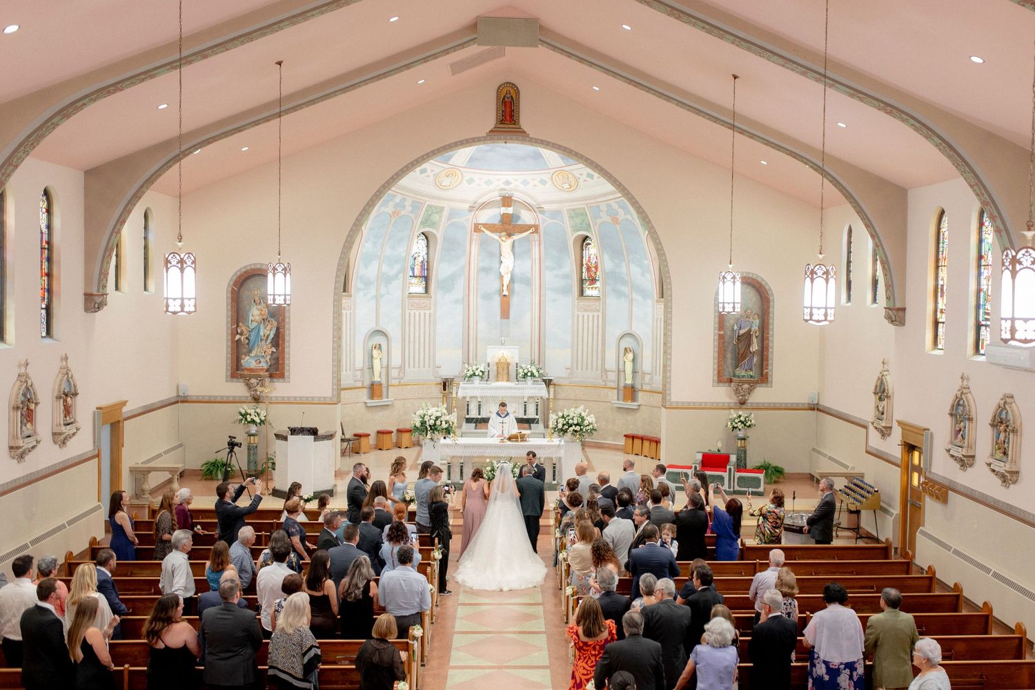 Elevated view of Catholic church wedding ceremony with guests filling wooden pews.
