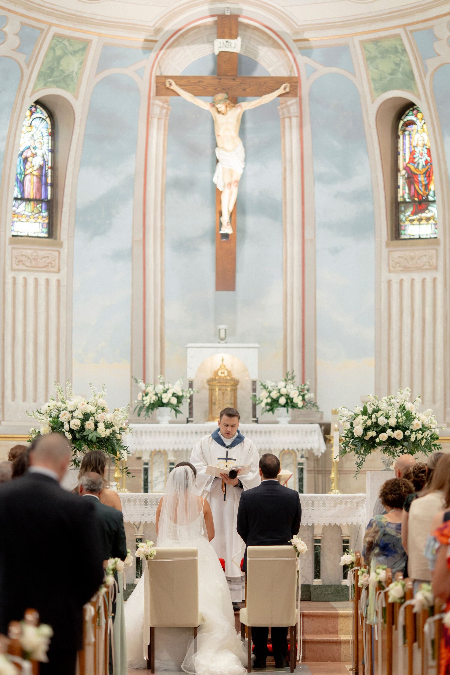 Catholic wedding ceremony in front of an altar with crucifix and white floral arrangements.