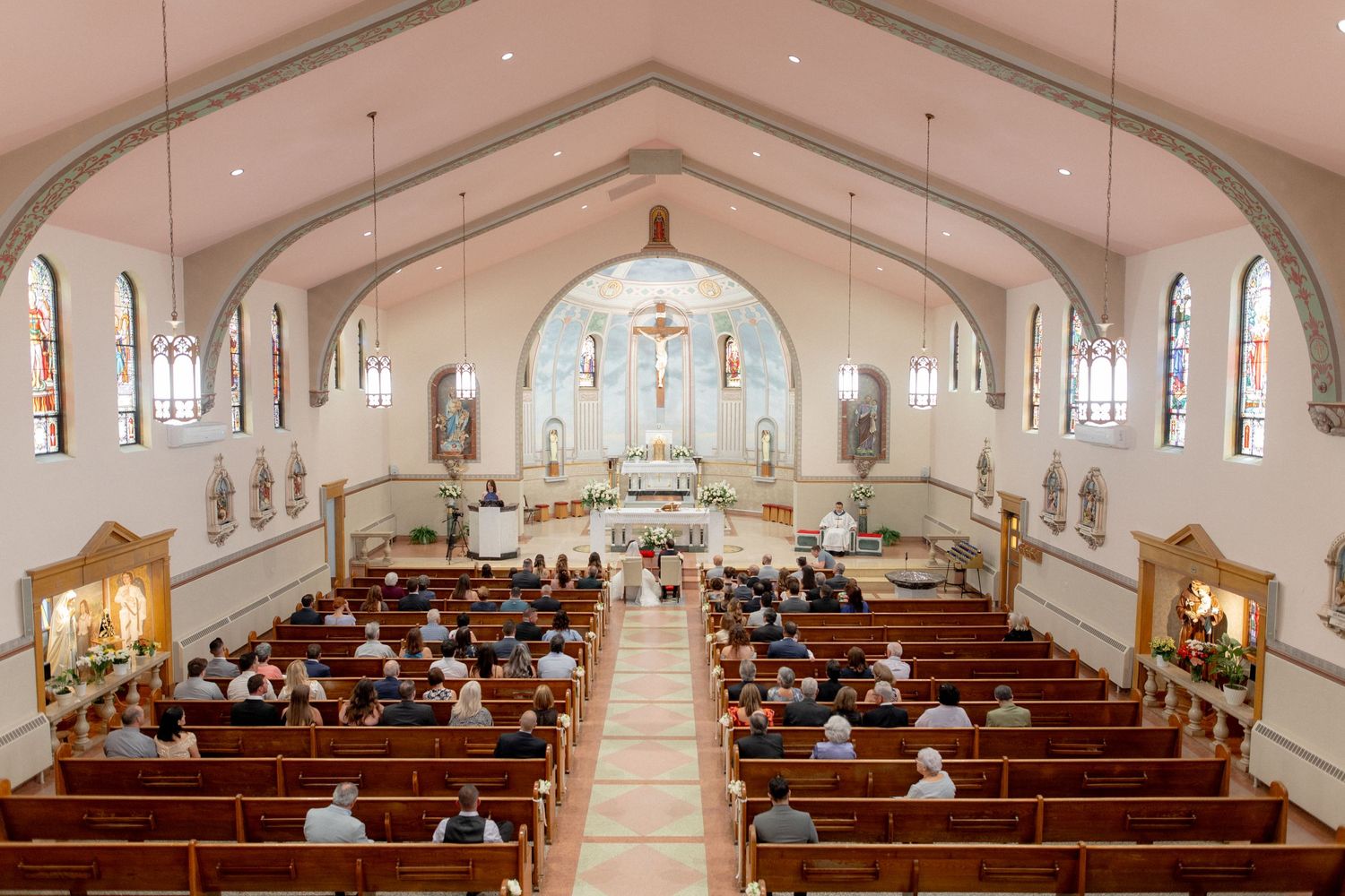 Bird's eye view of wedding ceremony in traditional Catholic church with arched ceiling and wooden pews.