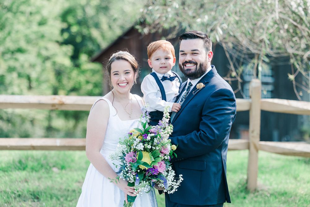 Wedding portrait of couple with young ring bearer in front of wooden fence.