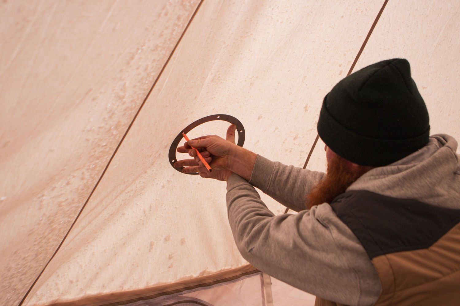 Person adjusting equipment inside canvas tent in warm lighting.