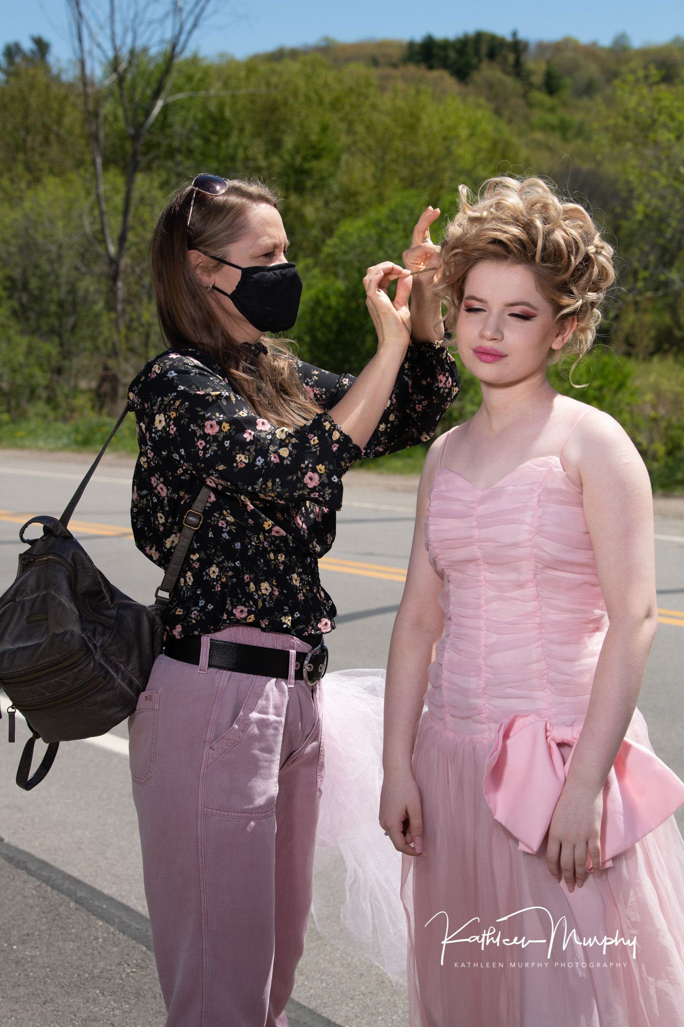 Behind the scenes of hair styling during outdoor photo shoot with pink formal dress.