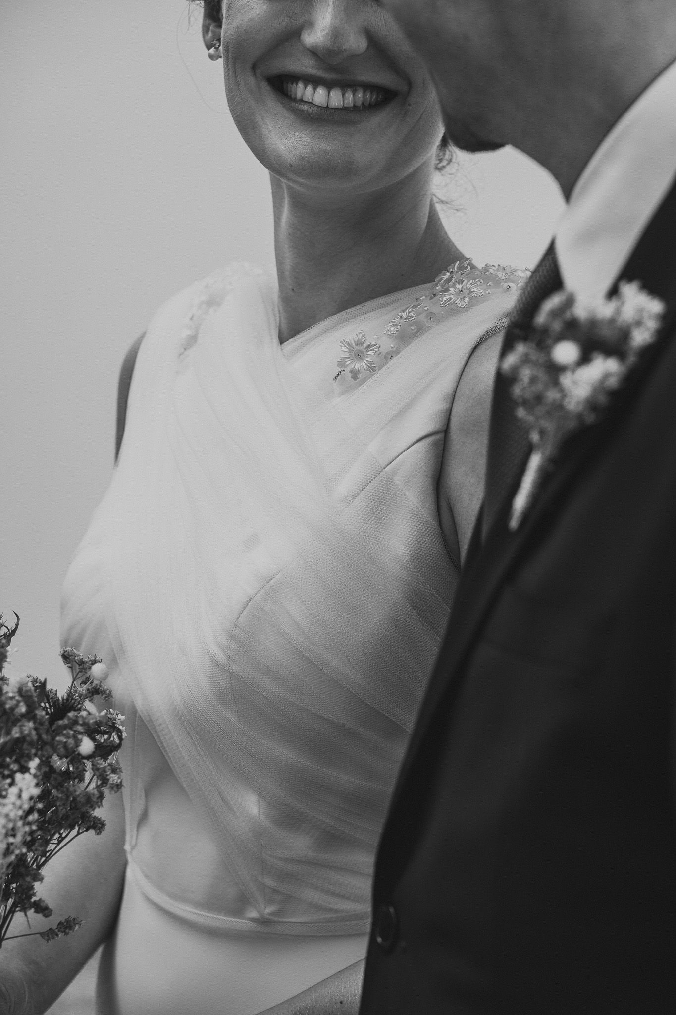 Close-up black and white photo of a wedding couple showing lace dress details and floral boutonniere.