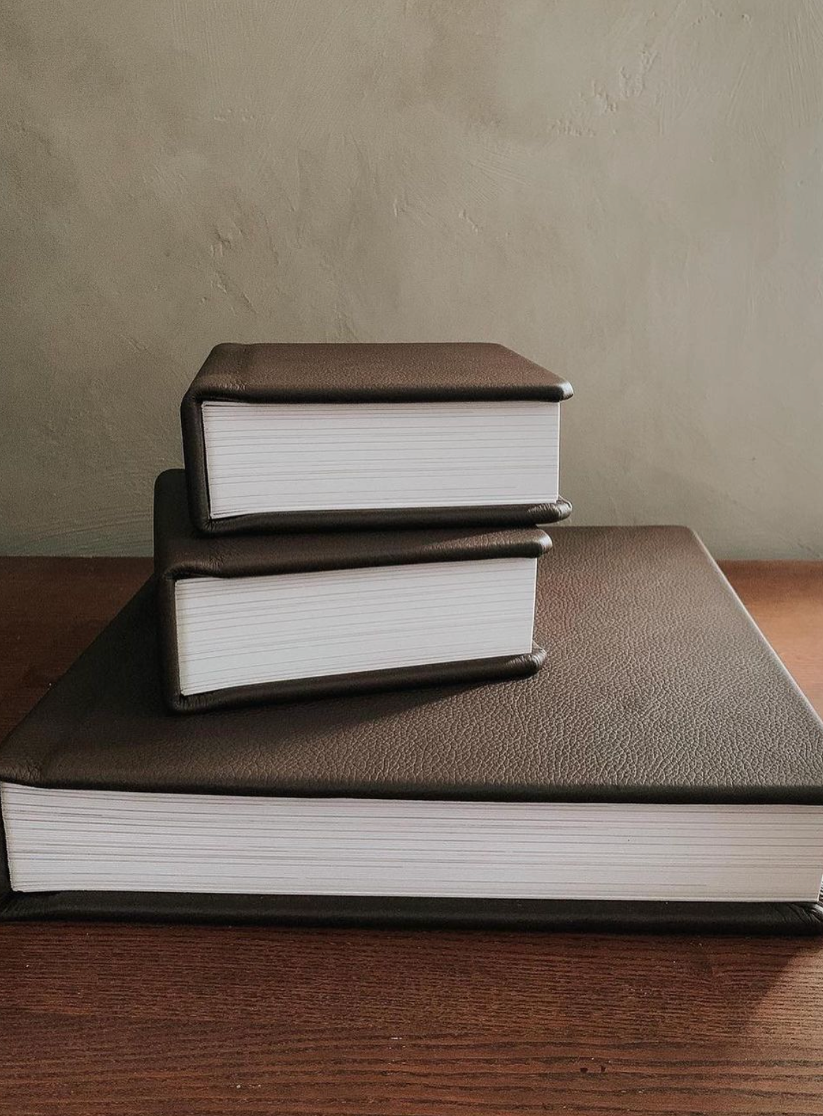 Stack of thick white hardcover books arranged on a brown textured surface.