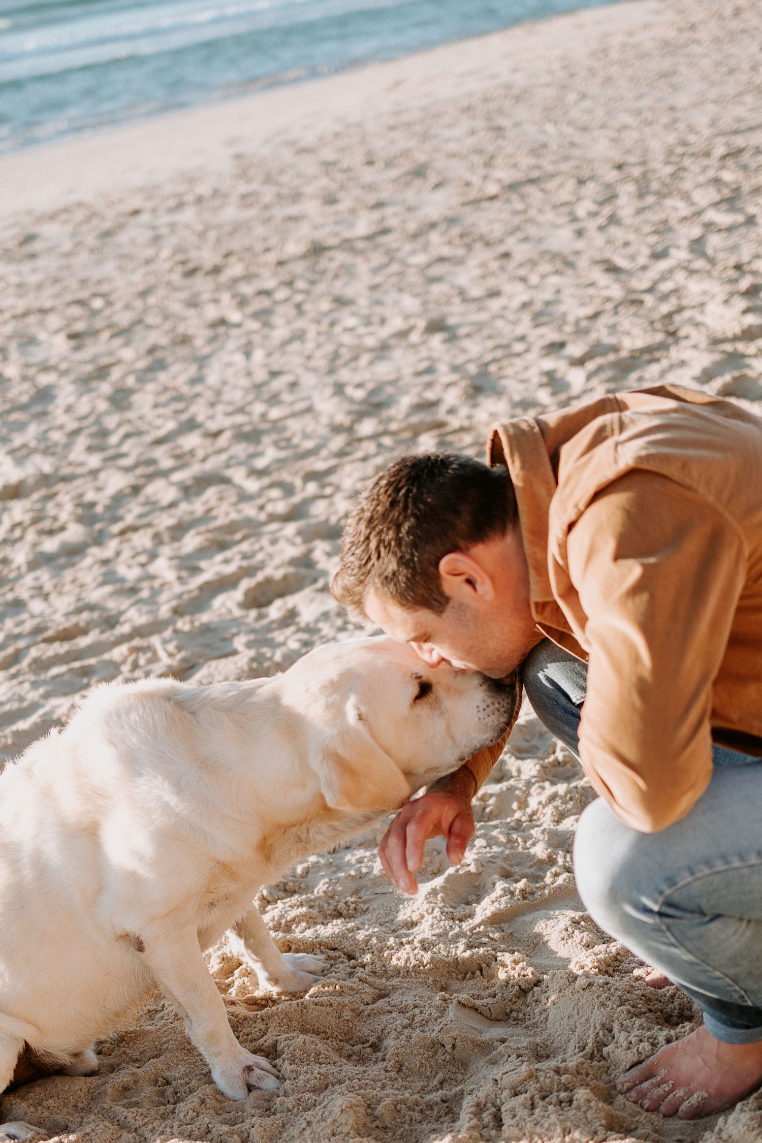 A person shares a tender moment with their white Labrador on the sandy beach.