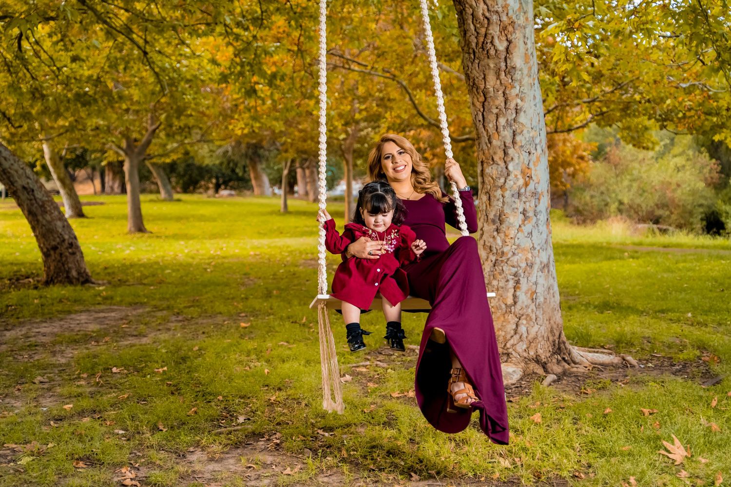 Family photoshoot on decorated tree swing surrounded by golden autumn foliage.