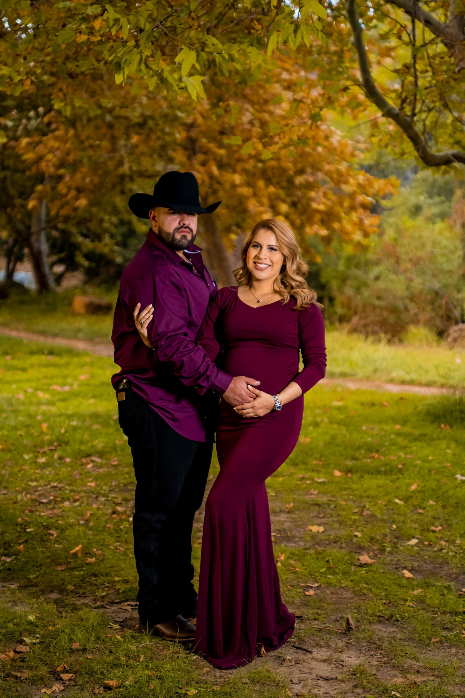 Elegant couple in coordinated burgundy outfits pose in autumn park setting.