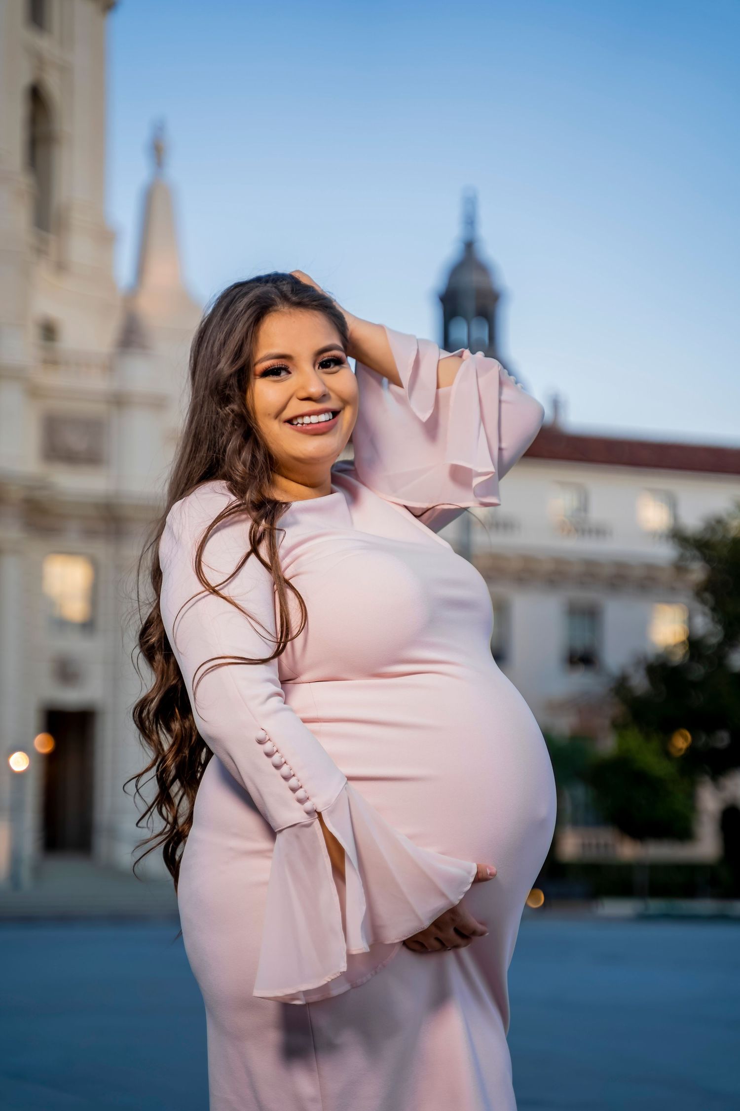 A maternity portrait showcasing an elegant pink dress against historic architecture.