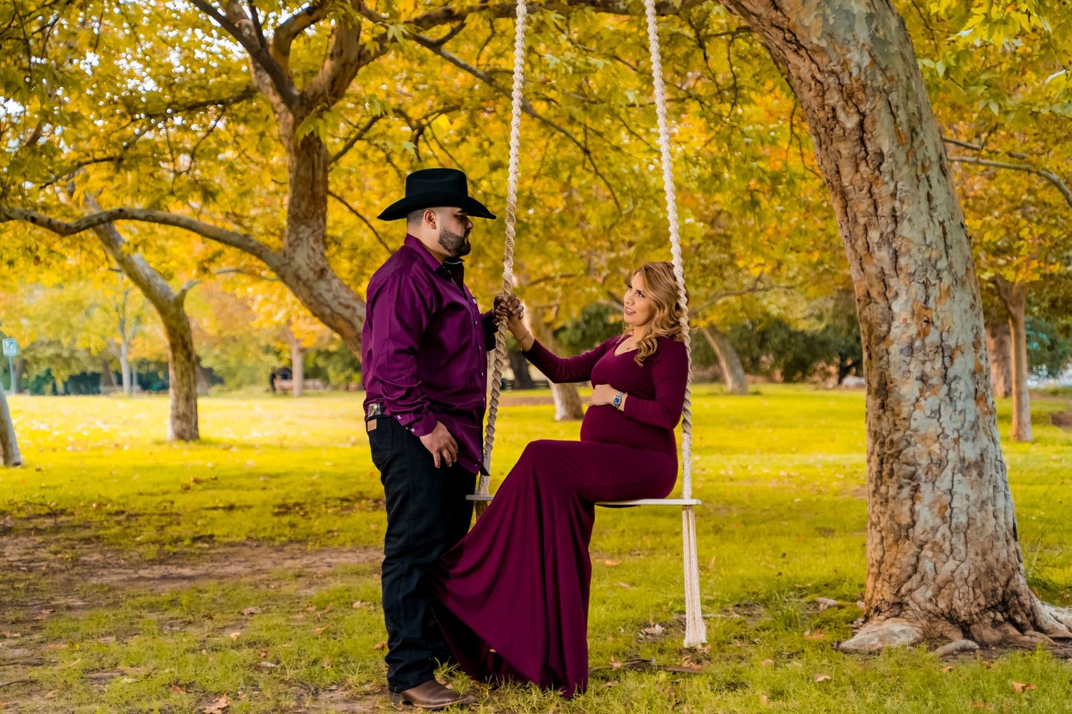 Couple in burgundy outfits enjoy romantic moment on tree swing during autumn.