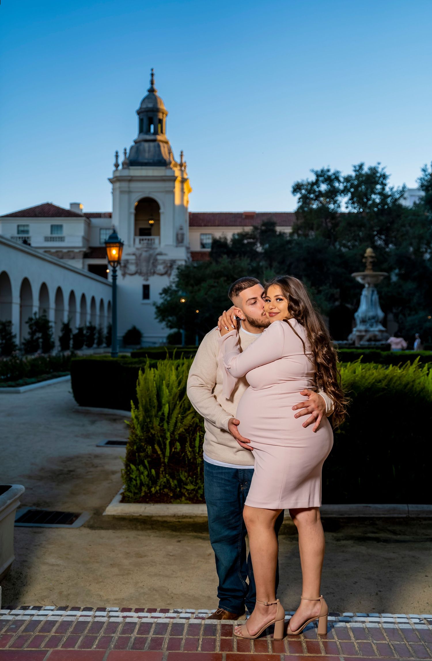 Evening maternity portrait with Spanish colonial architecture and manicured gardens in background.