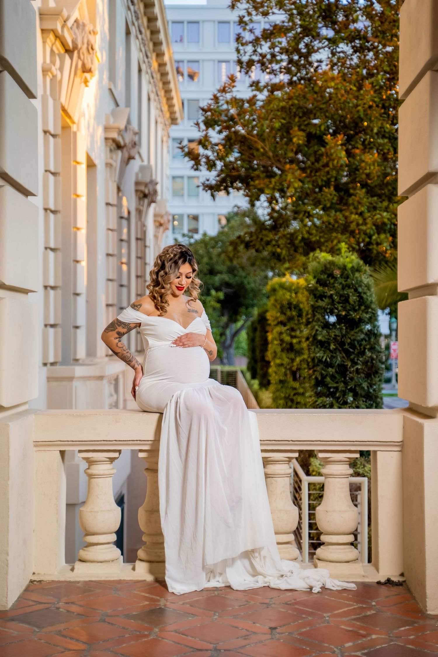 A maternity portrait on a classical balcony with stone columns and architectural details.