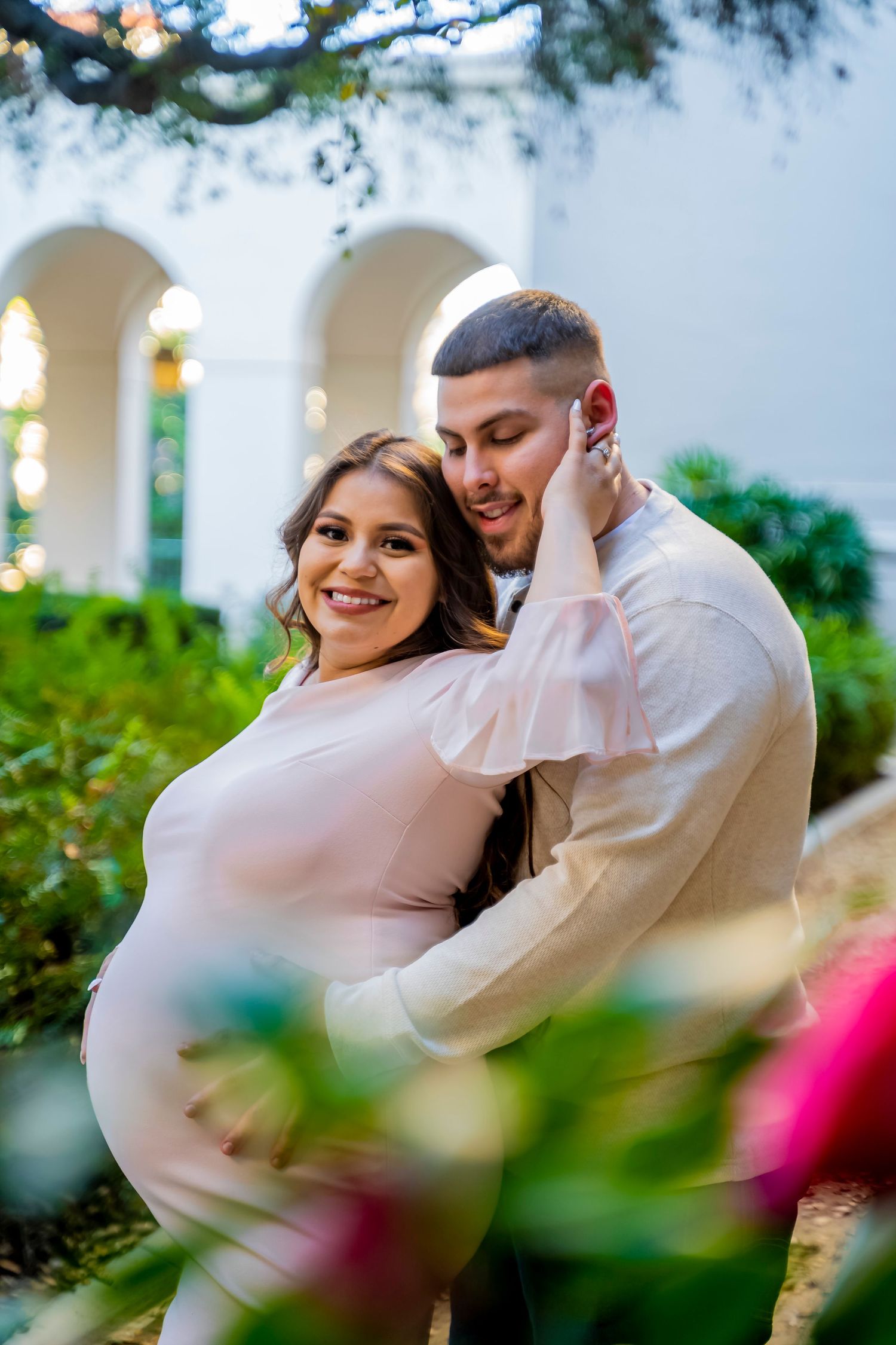 A maternity photoshoot in a garden setting with white arches and blooming flowers.