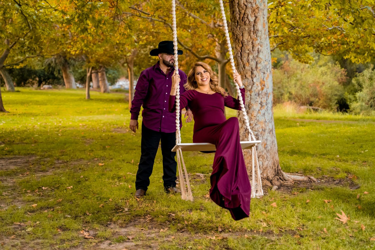 Romantic autumn scene with couple in matching burgundy outfits on tree swing.