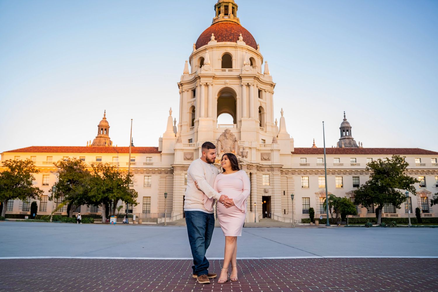 A maternity photo captured in front of Pasadena City Hall's grand facade at sunset.