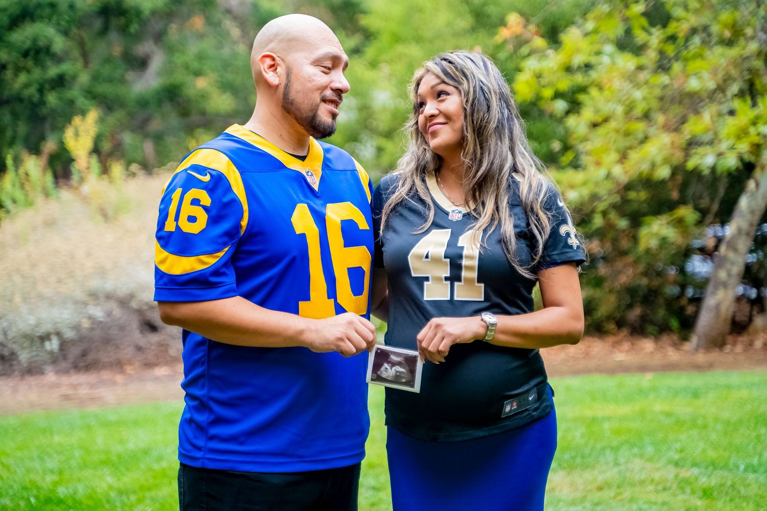 Couple in sports jerseys sharing a laugh during pregnancy announcement photoshoot.