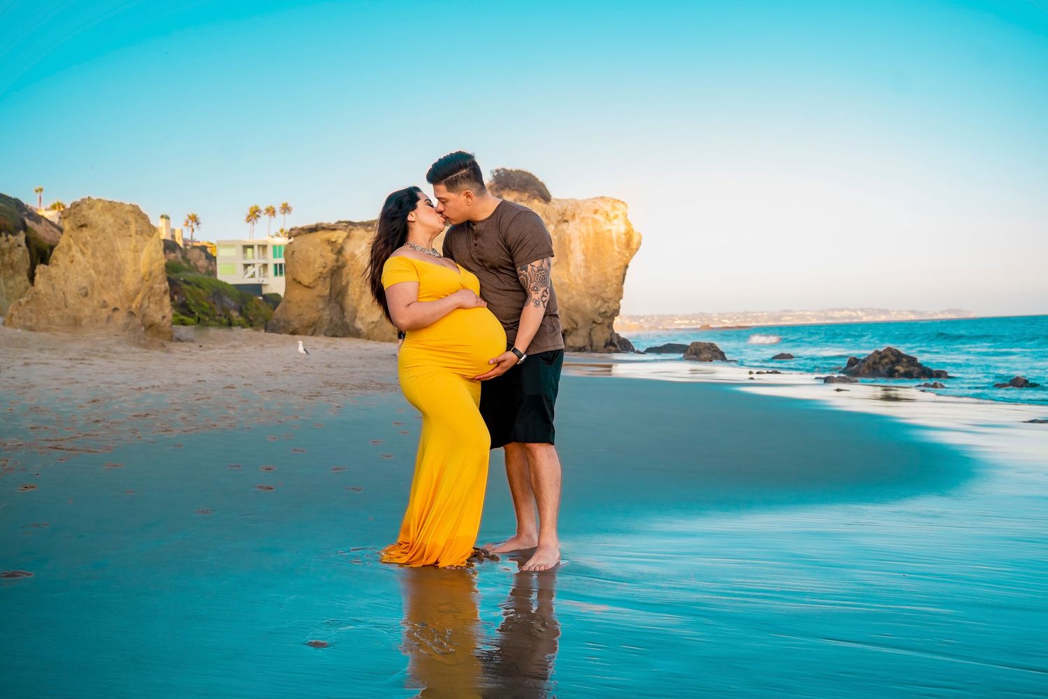A maternity photo shoot at sunset on a beach with coastal cliffs in the background.