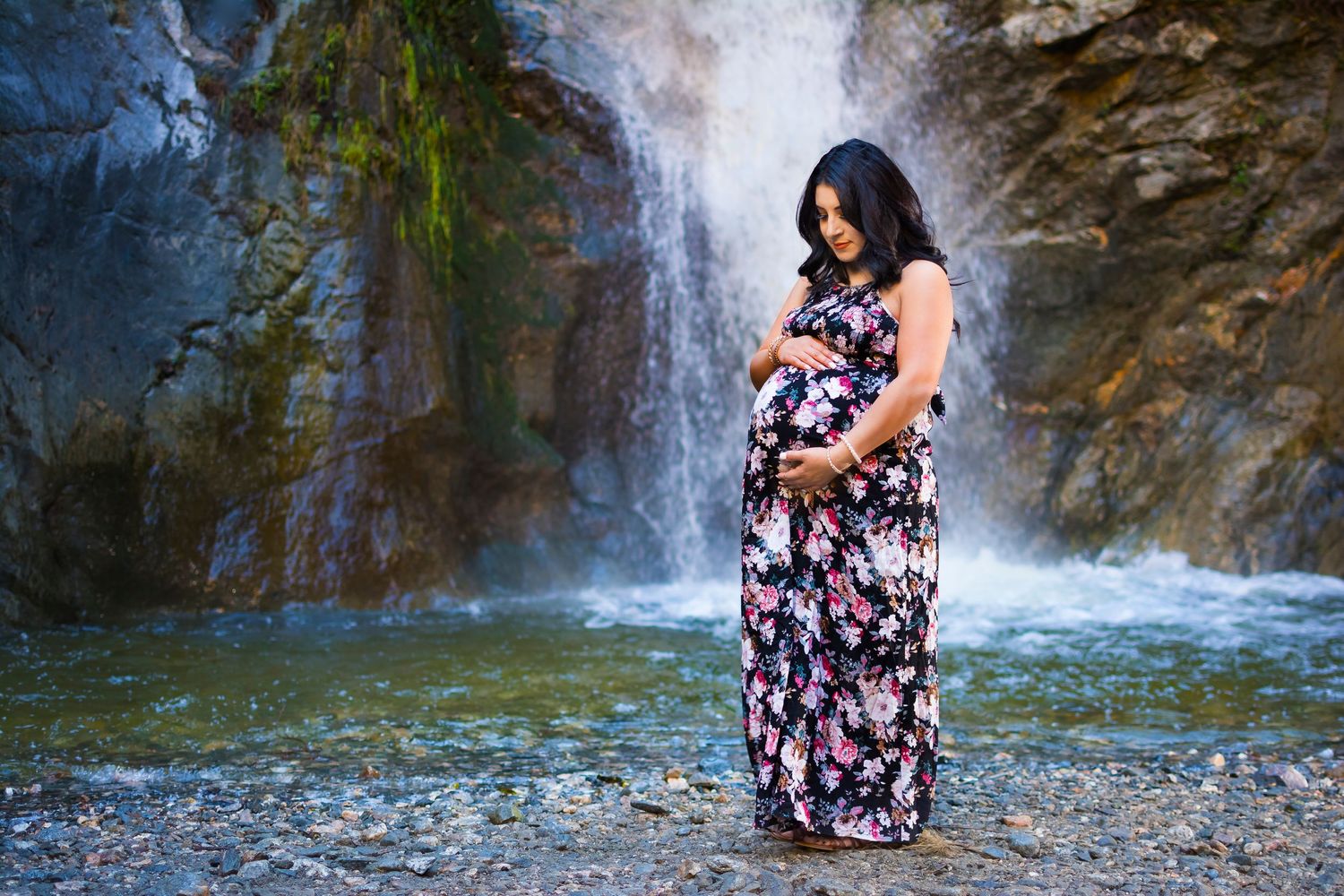 A maternity portrait against a scenic waterfall and rocky landscape.
