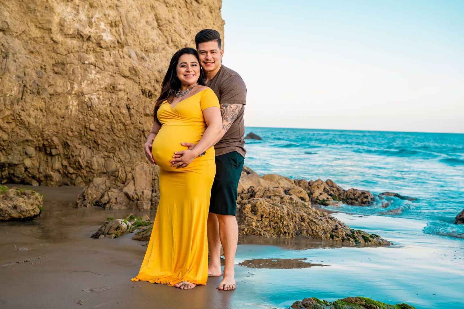 A maternity photo shoot featuring a yellow dress against dramatic coastal scenery.