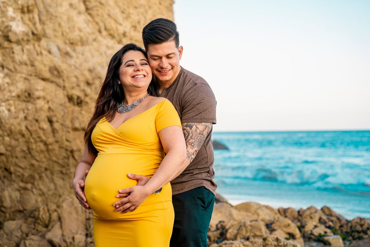 A beachside maternity portrait with turquoise ocean waves and rocky cliffs.